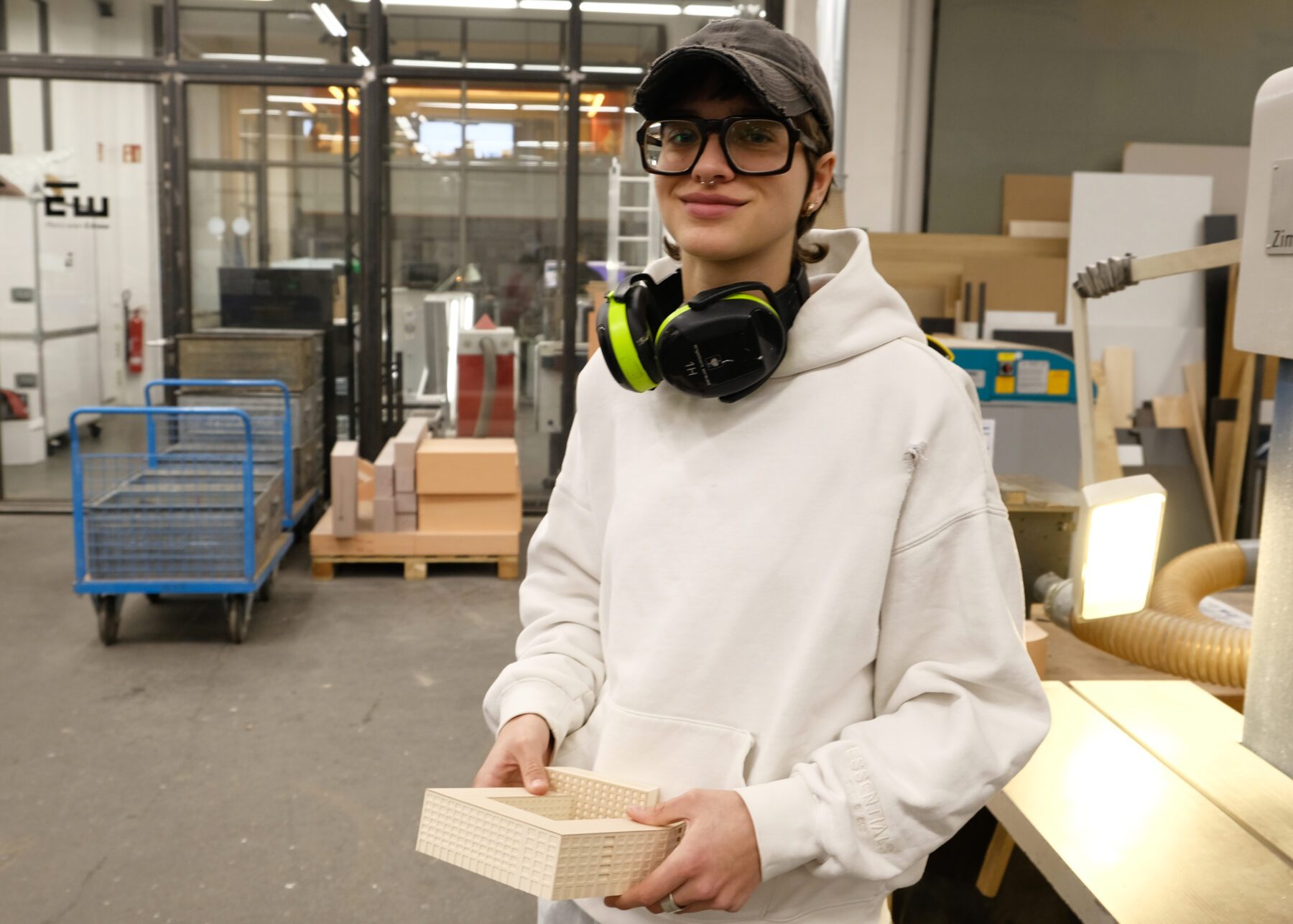 Portrait von Emma Sulzmann in der Maschinenhalle bei werk5. Sie trägt ein schwarzes Basecap eine Brille und einen weissen Hoody.