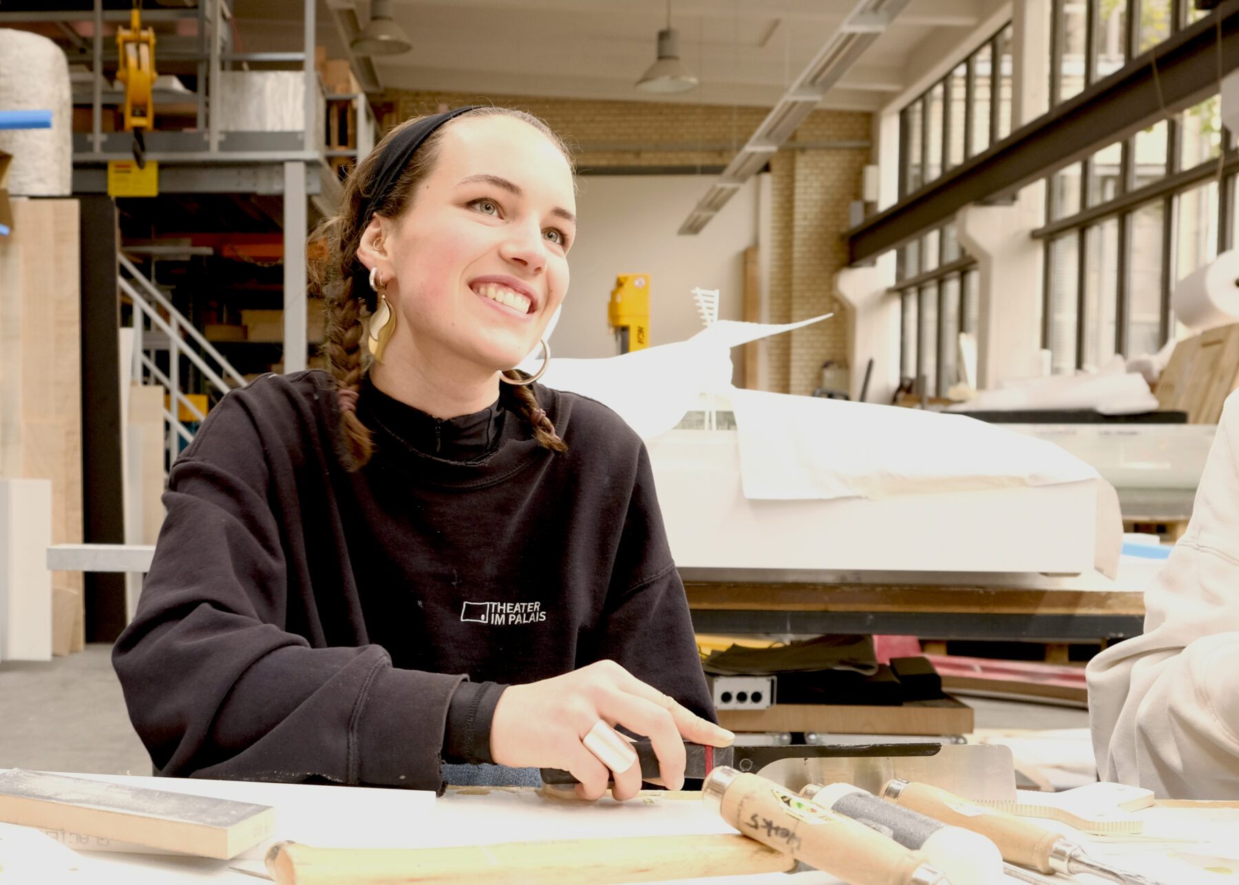 Portrait von Hannah Ruetten - Auszubildende bei werk5 in Berlin. Sie hat geflochtene Zöpfe und trägt einen schwarzen Pullover